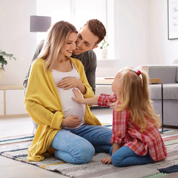 Young parents with a little girl holding her hand on the mothers pregnant stomach on their knees happy to be having a baby